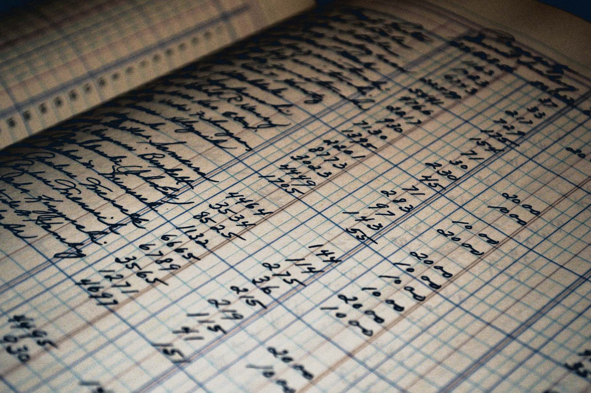 A handwritten columned ledger page in warm light, shallow focus.
