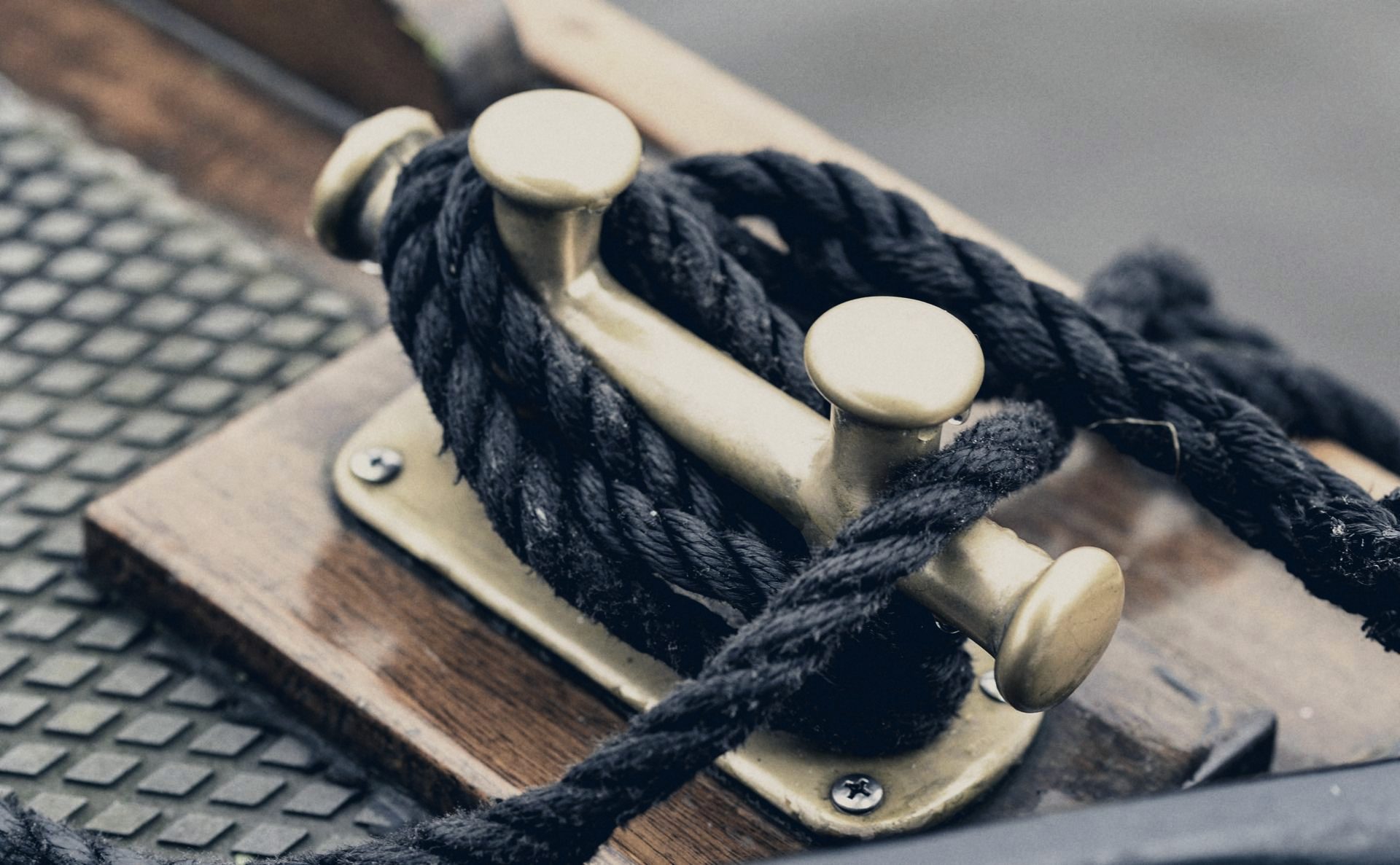 A dark rope made fast around a brass cleat on a varnished wooden deck.
